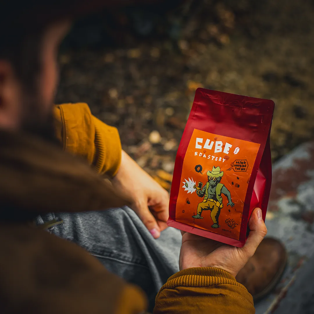 Pachet de cafea CUBE Roastery ținut în mână într-un cadru exterior.