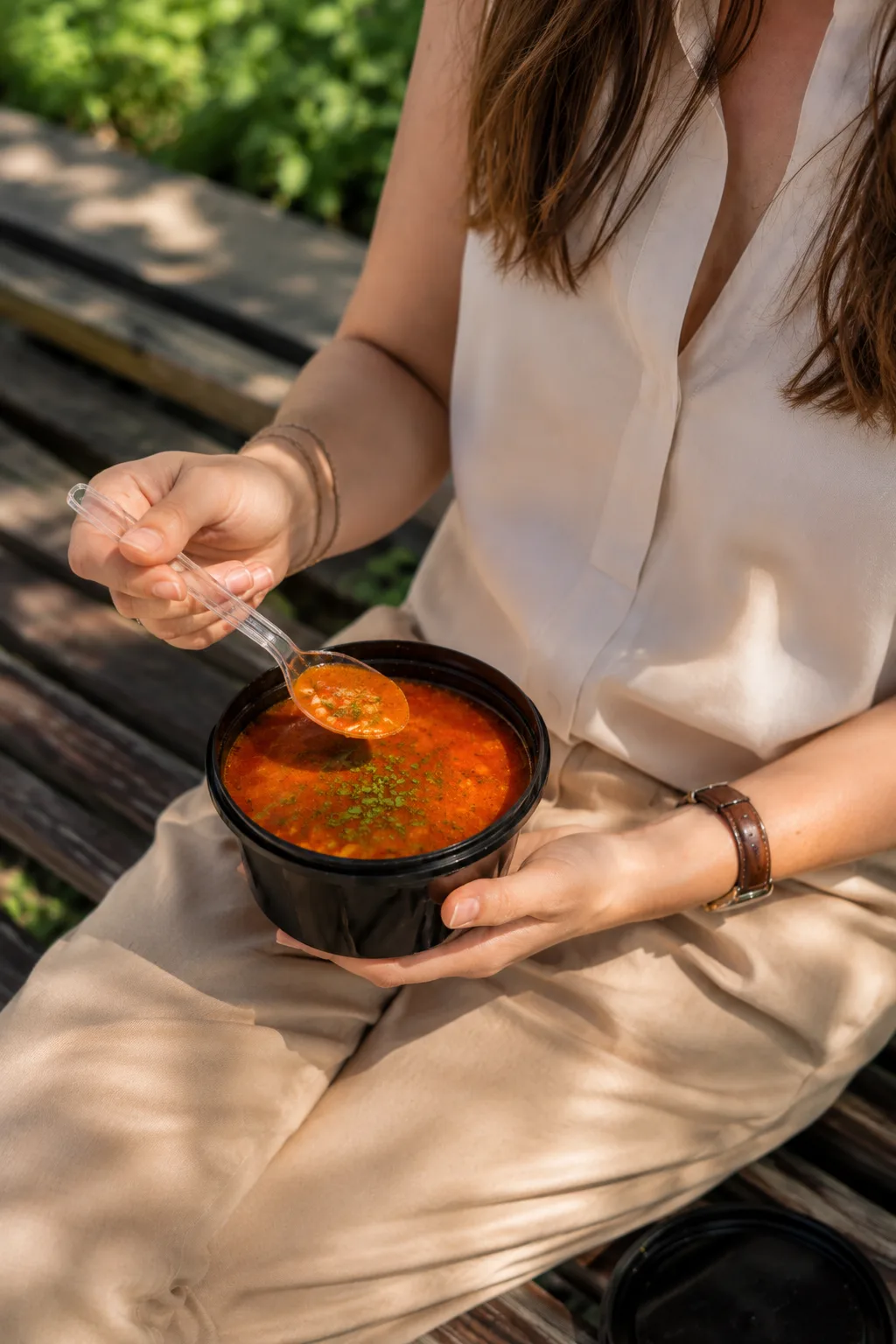 Persoană care ține un bol real de ciorbă GET EAT într-un cadru exterior.